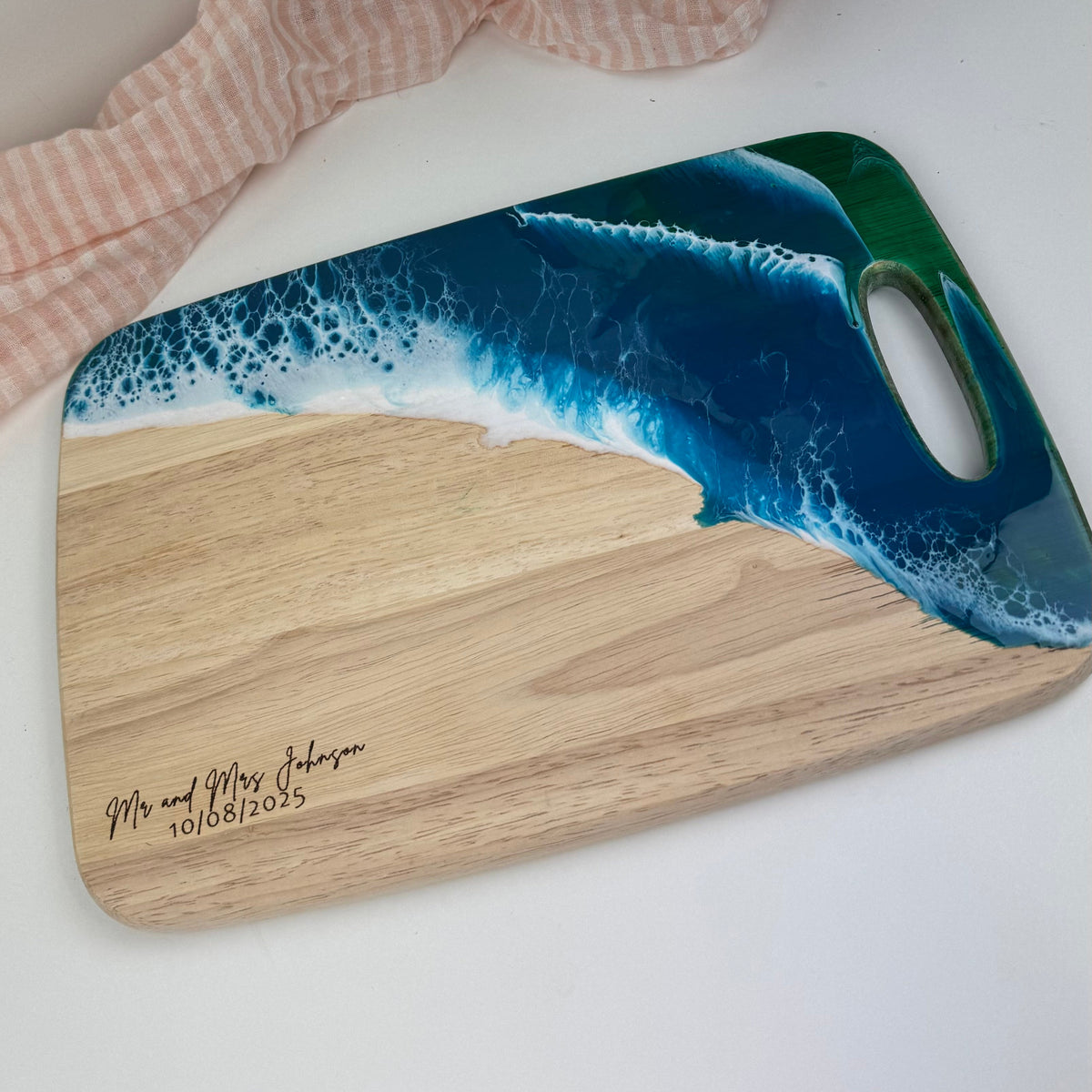 Wooden cutting board with ocean design and engraved text on a white surface.