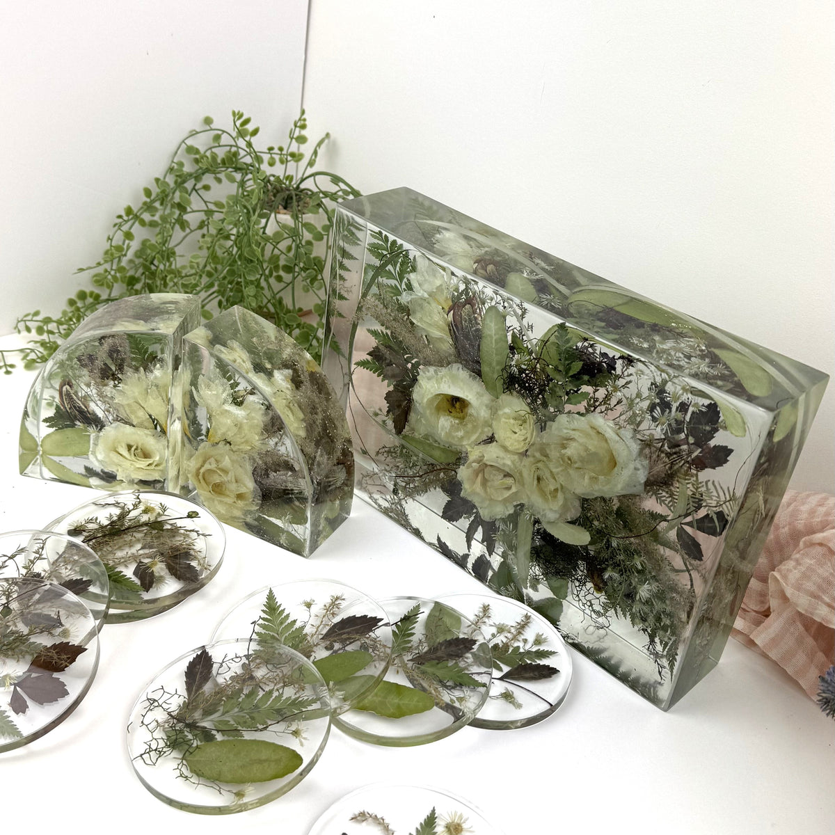 A set of clear resin keepsake boxes and round coasters containing pressed flowers and green leaves, displayed on a white surface with a white background.