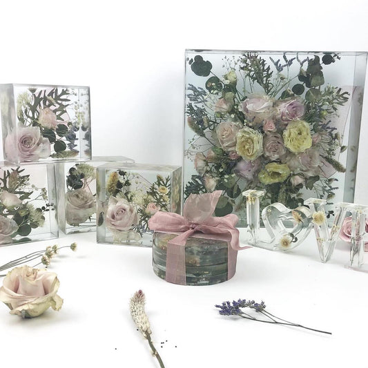 A collection of various bouquets and floral arrangements displayed in different sized clear resin, with a pink bow in the foreground.